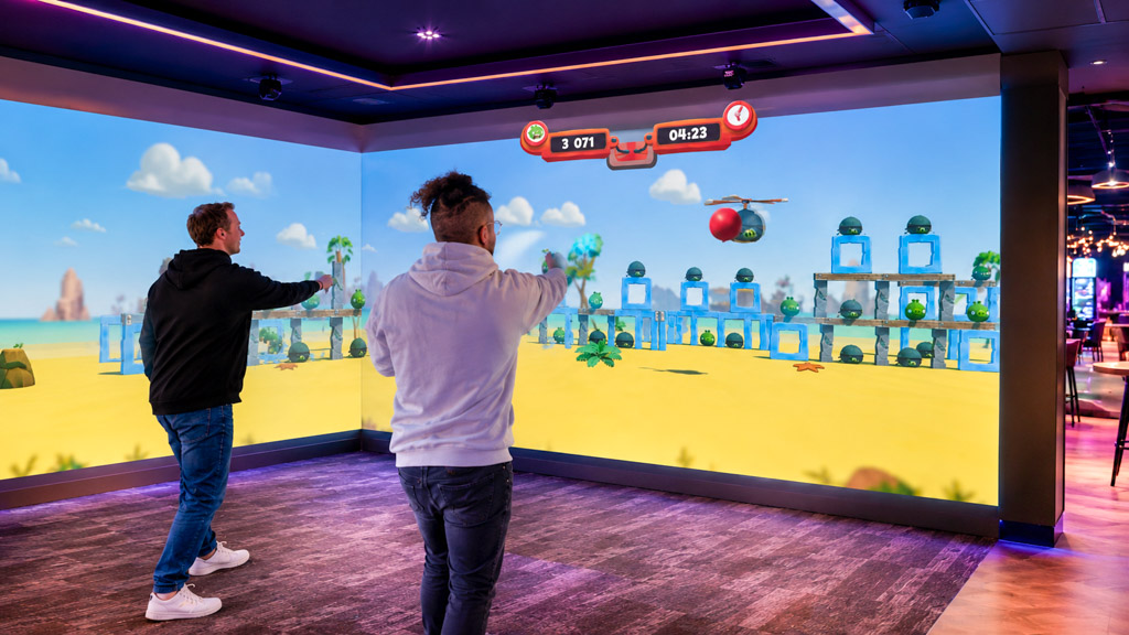 Twee bezoekers spelen een interactief spel op een grote NeoXperiences projectiewand in een modern Family Entertainment Center.